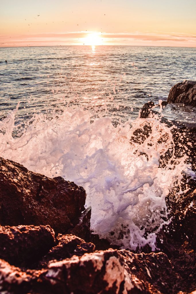 Wave crashing on shore with sunset in the background